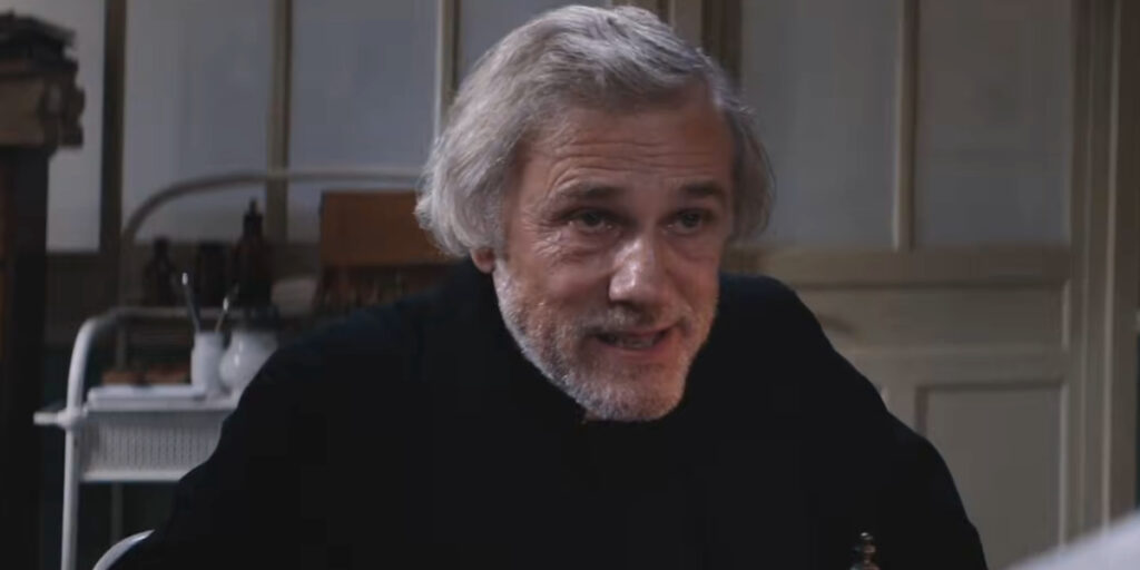 Christoph Waltz shown sitting in a hospital in urgent conversation in Dracula.