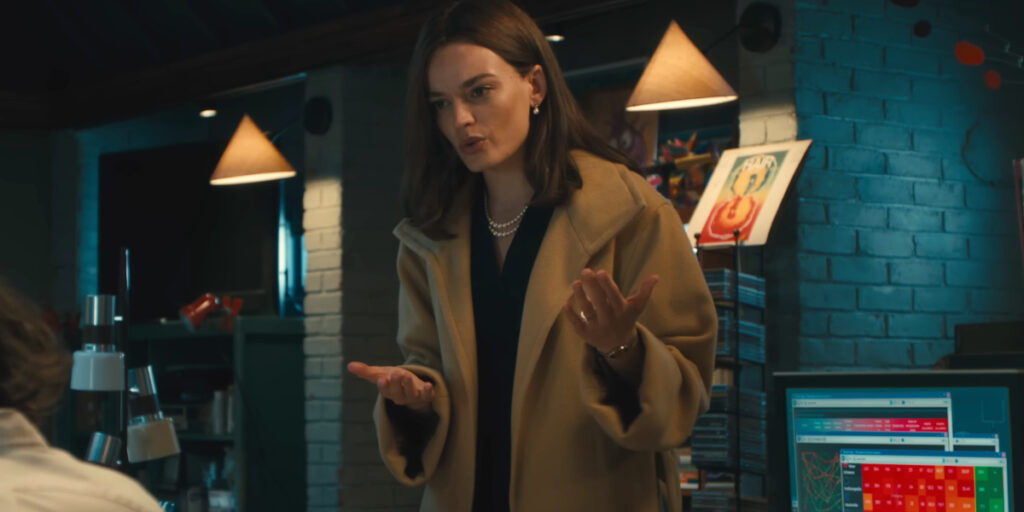 Emma Mackey passionately stands in mid-speech in an office in Ella McCay,