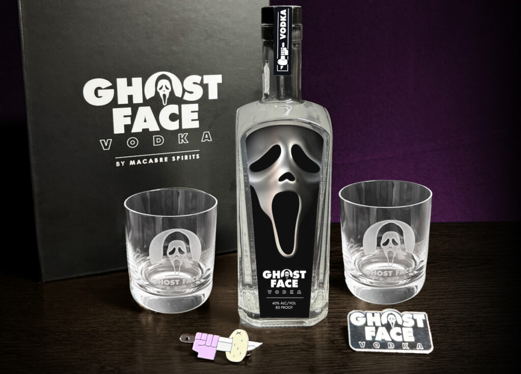 A bottle of Ghost Face Vodka, shown with two collector's glasses, a pin, and a logo piece, for the Ghost Face Vodka Collectable Box.