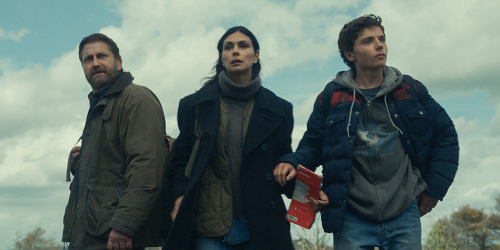 Gerard Butler, Morena Baccarin, and Roman Griffin Davis stand together bundled up outdoors in Greenland 2: Migration.