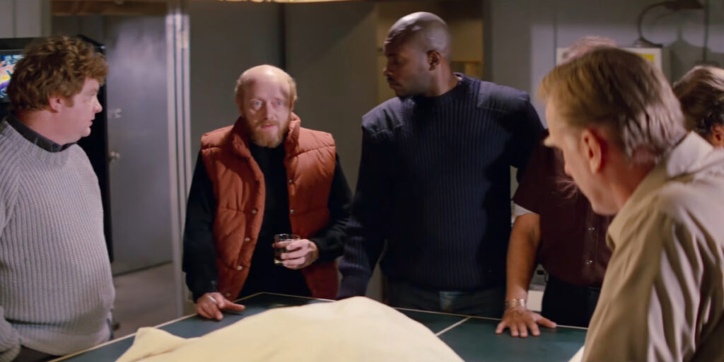 Members of the outpost crew stand around an examining table in The Thing.