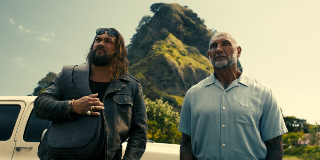 Jason Momoa and Dave Bautista stand together in front of a lush mountain in The Wrecking Crew.