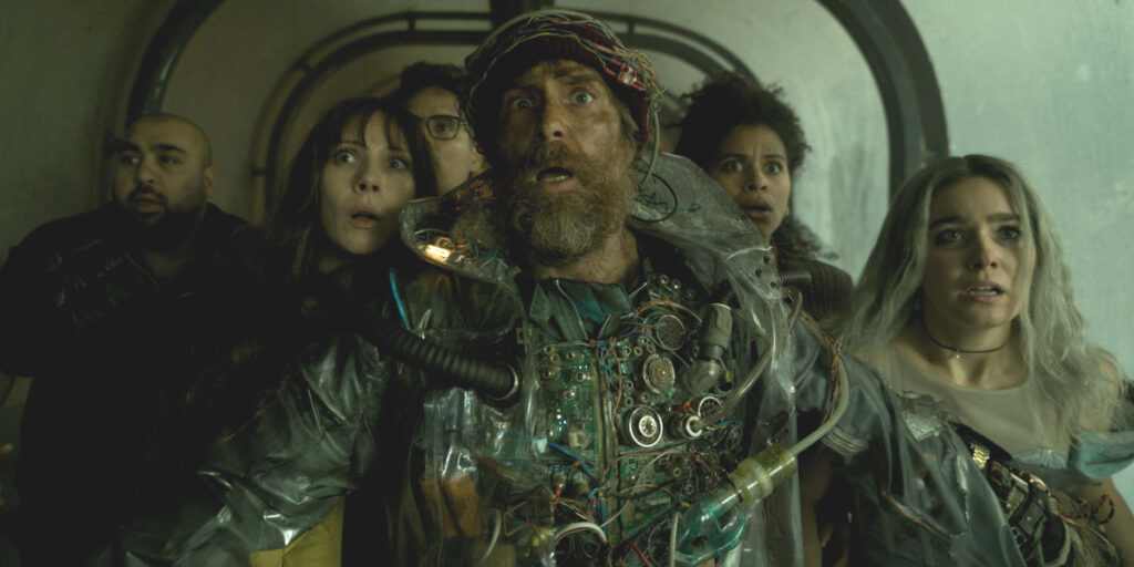 A frightened Sam Rockwell stands in front of a group of similarly terrified castmates in Good Luck, Have Fun, Don't Die.