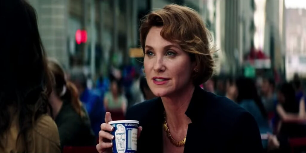 Judith Hoag leans over in conversation with Megan Fox while holding a coffee cup in Teenage Mutant Ninja Turtles: Out Of The Shadows.
