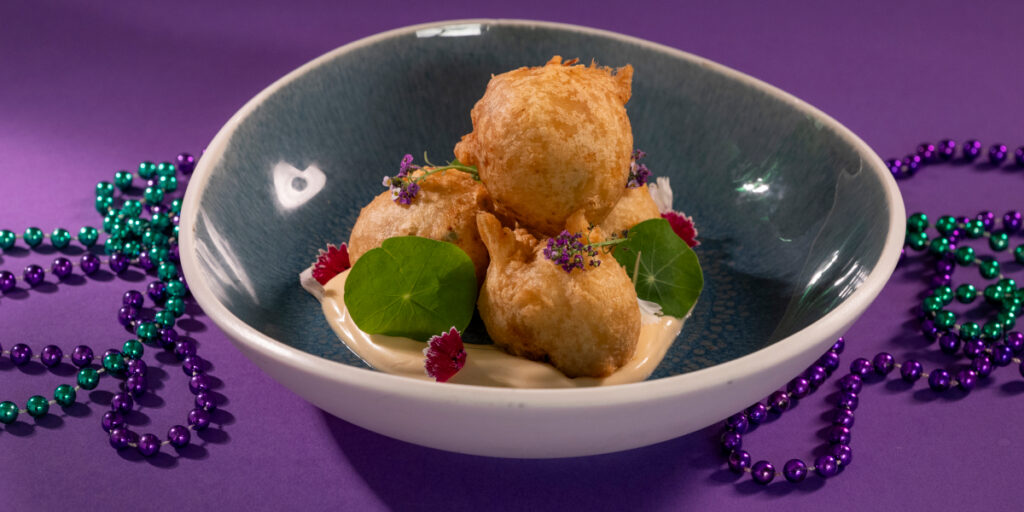 Soul Crab Beignets shown plated and surrounded by beads, for Universal Mardi Gras 2026.