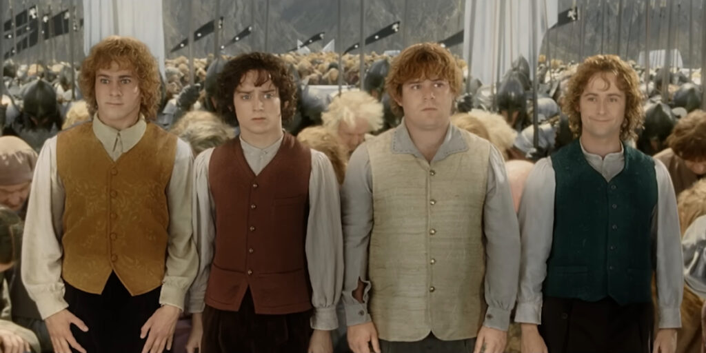 Dominic Monaghan,  Elijah Wood, Sean Astin, and Billy Boyd stand lined up at the coronation of Aragorn in The Lord of the Rings: The Return of the King.