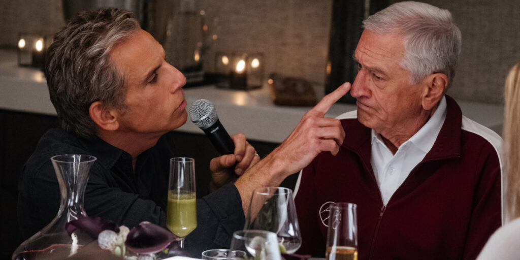 Ben Stiller speaks on a mic while trying to boop a stern Robert De Niro's nose in Focker-In-Law.