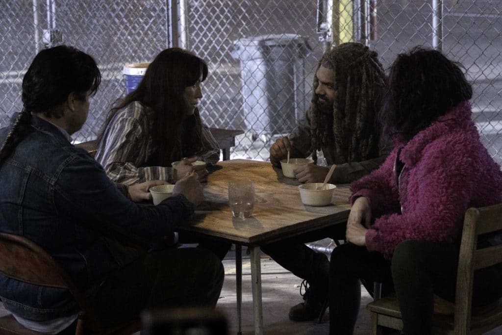 The Walking Dead season 11 photo of Ezekiel, Yumiko, Princess, and Eugene sitting at a table in a fenced holding pen.